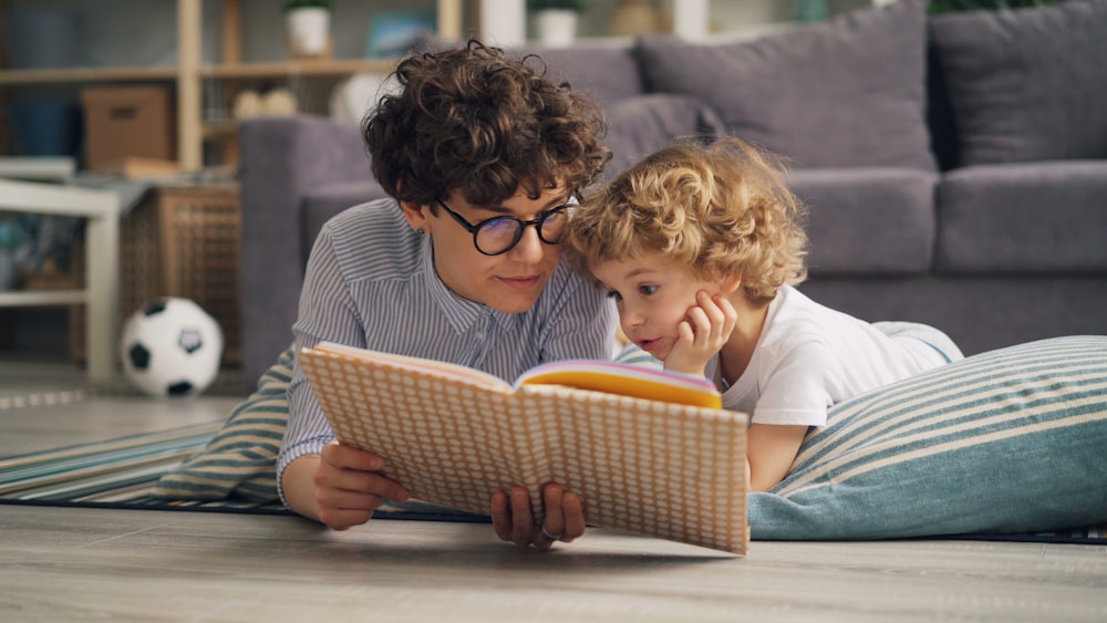 A parent and a young child reading a picture book together on the floor.